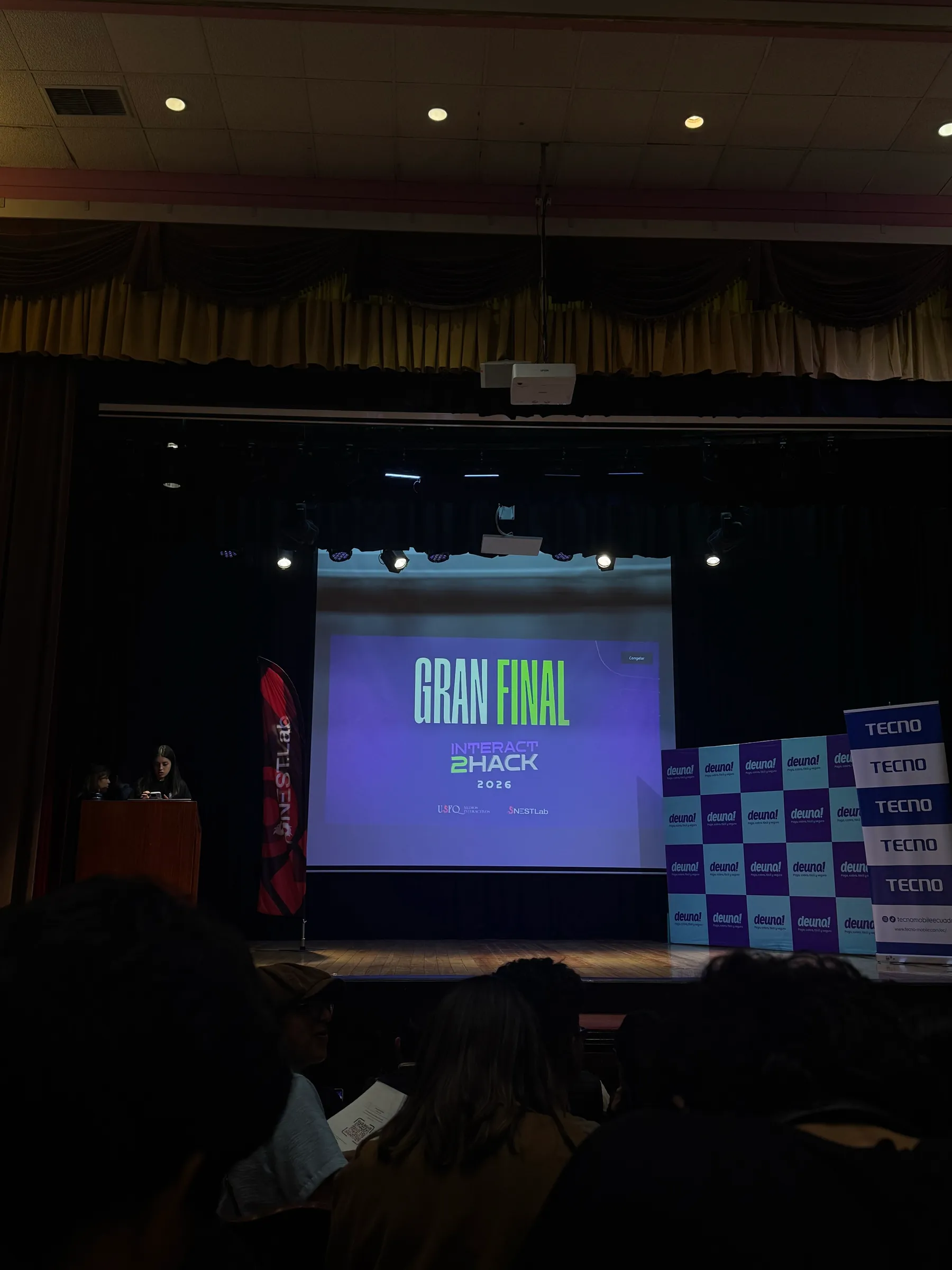 A stage screen reading 'Gran Final, Interact2Hack 2026' at the USFQ auditorium