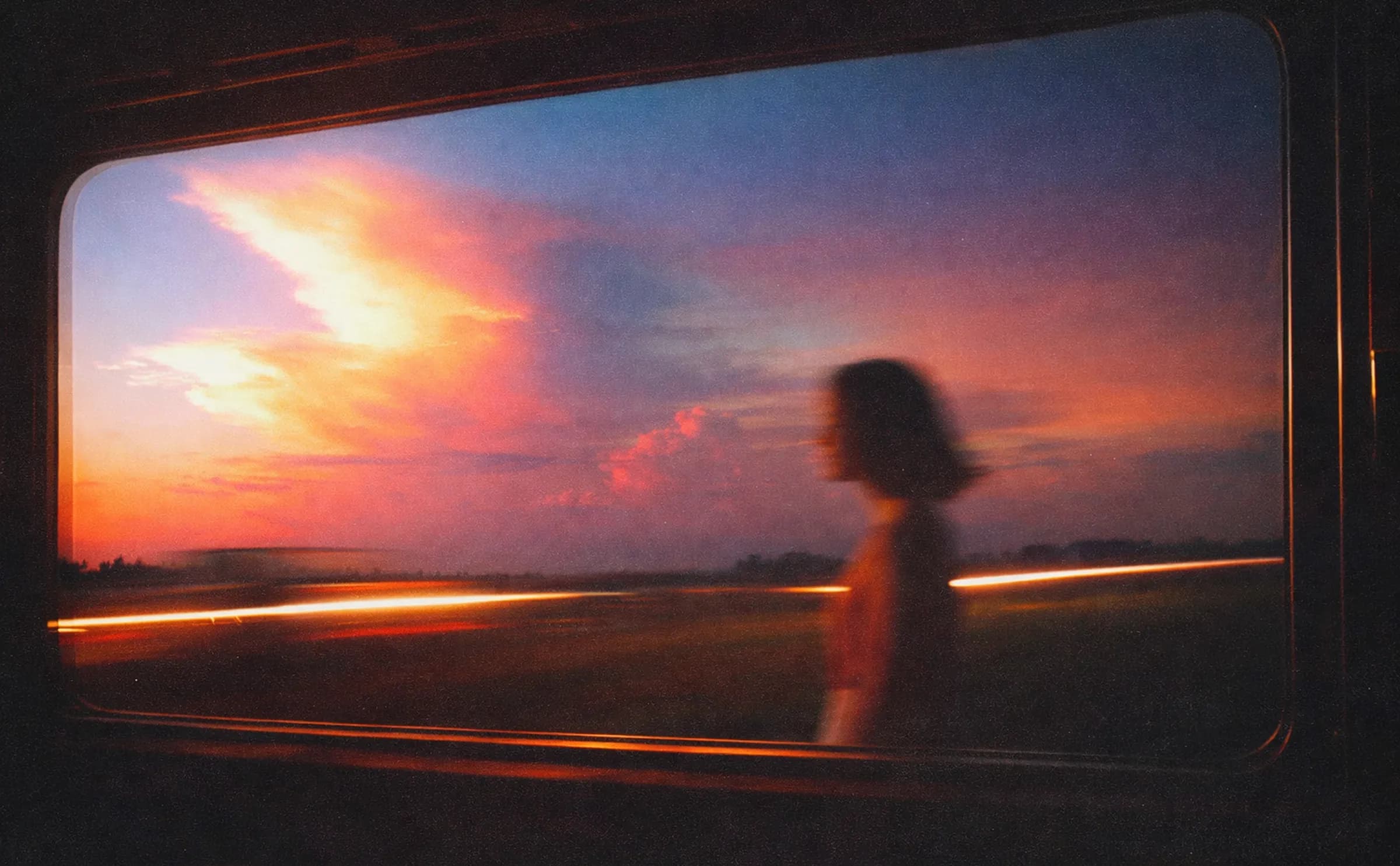 A train window at sunset, a figure passing in front of the racing lights