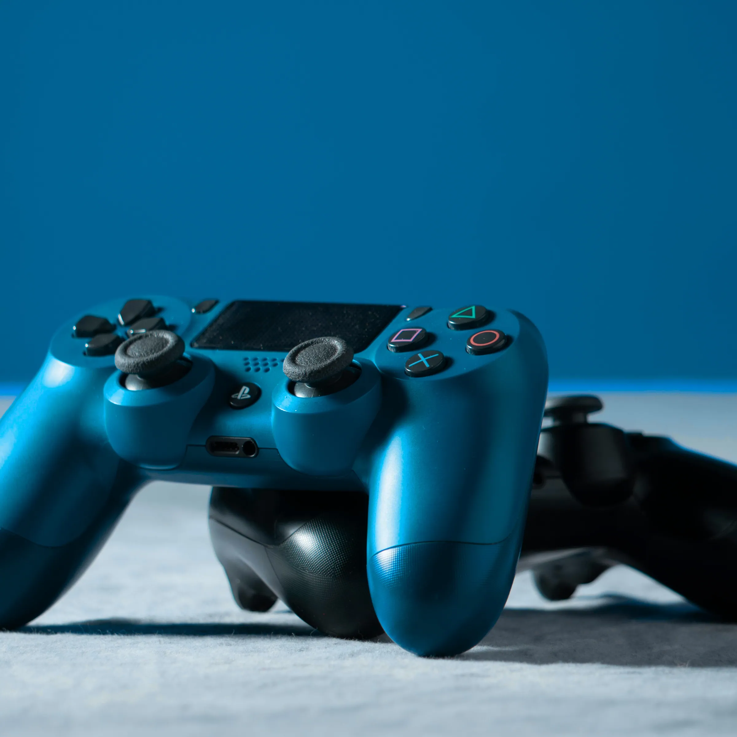 Two game controllers, one deep blue, on a blue backdrop