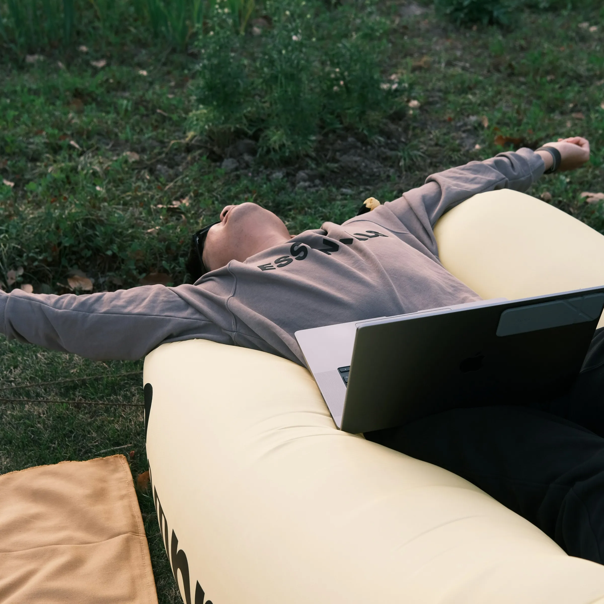 A student stretched out on a lounger in the park, laptop on his lap