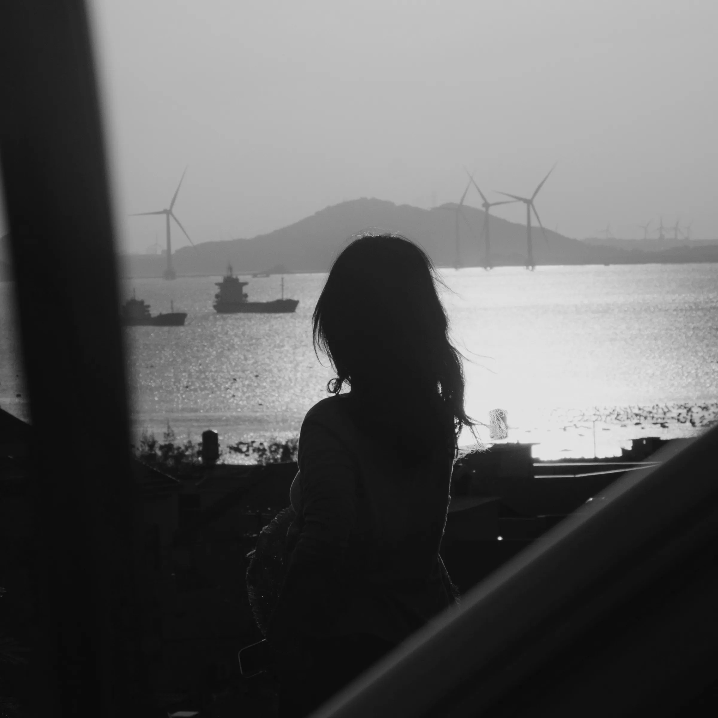 A silhouette looking out over the sea, wind turbines on the horizon
